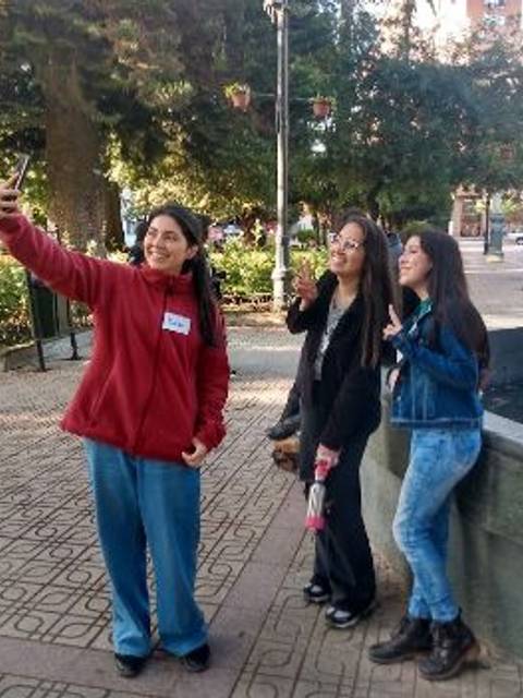 Un grupo de tres jóvenes sonríen mientras se toman una selfie en un parque.