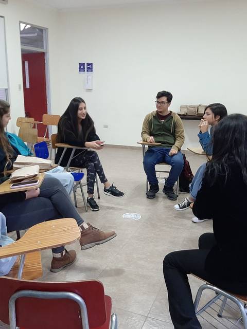 Un grupo de seis personas está sentados en sillas en un aula, participando en una conversación en círculo.