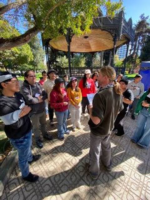 Un grupo de personas escuchando a un hombre que habla en un parque.