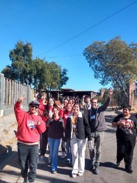 Un grupo de personas sonrientes camina por una calle al aire libre, levantando las manos en señal de alegría.