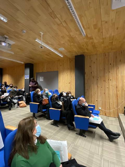 Una conferencia en un auditorio con varias personas sentadas y un ponente de pie presentando.