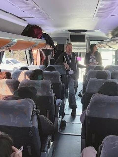 El interior de un autobús con varios pasajeros sentados y dos personas de pie al frente.