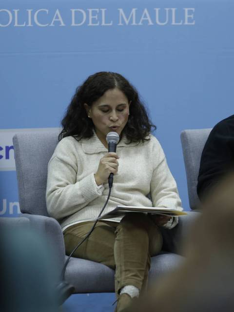 Una mujer está sentada en un panel, sosteniendo un micrófono mientras habla.