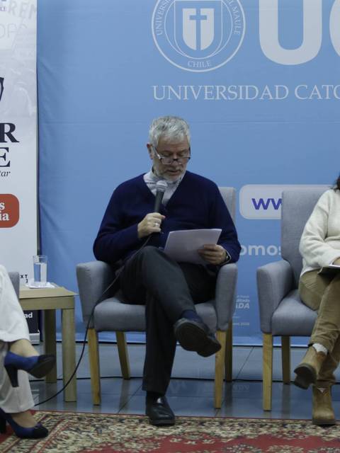 Un panel de discusión en la Universidad Católica del Maule, con varios ponentes sentados en sillas.