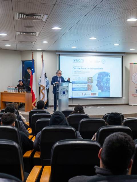 Una conferencia se lleva a cabo en un auditorio con una presentación en pantalla.