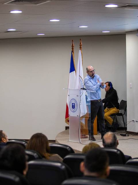 Un hombre presenta información frente a un público en una sala de conferencias.