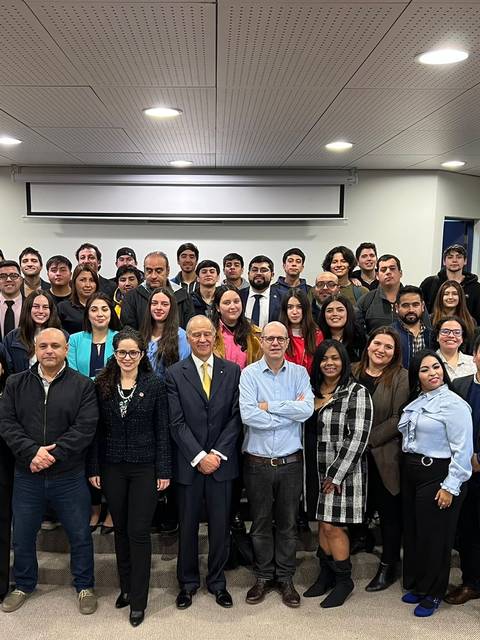 Grupo de personas posando en un evento en un salón con banderas.