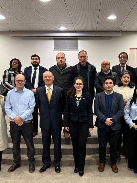 Un grupo de personas posando en un evento formal con fondo institucional.