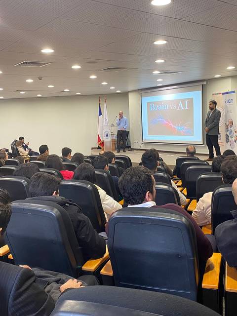 Una conferencia sobre inteligencia artificial con un presentador en el escenario y una audiencia atenta.