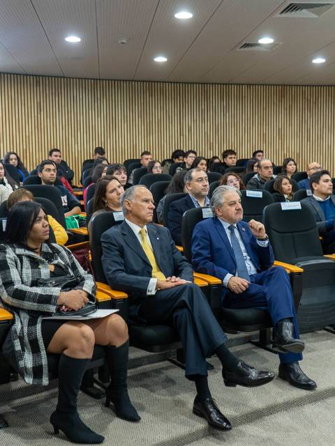 Una audiencia sentada en un salón, prestando atención a una presentación.
