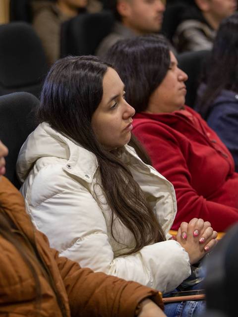 Un grupo de personas sentadas en una sala, prestando atención a una presentación.