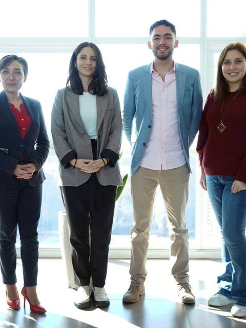 Un grupo de seis personas posando frente a una ventana con luz natural en un ambiente de oficina.