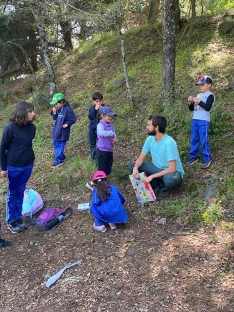 Un grupo de niños y adultos están reunidos en un entorno natural, conversando y jugando.