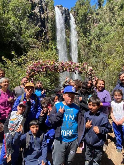 Un grupo de personas sonrientes posando frente a una hermosa cascada en un entorno natural exuberante.