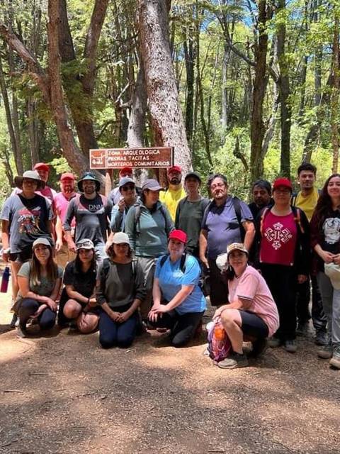 Un grupo de personas se reúne en un bosque, posando frente a un cartel informativo.