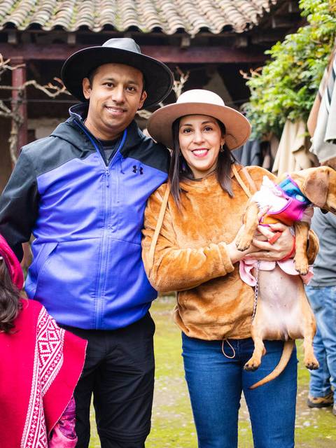 Una familia sonriente posando en un lugar al aire libre con un perro en brazos.