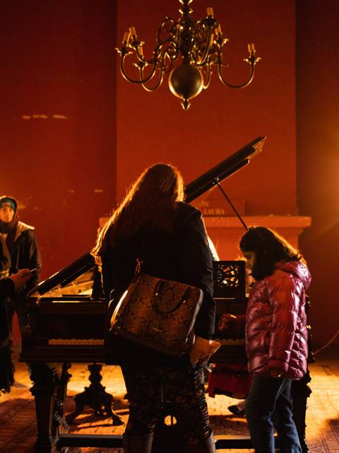 Un grupo de personas se reúne en una habitación iluminada donde hay un piano.