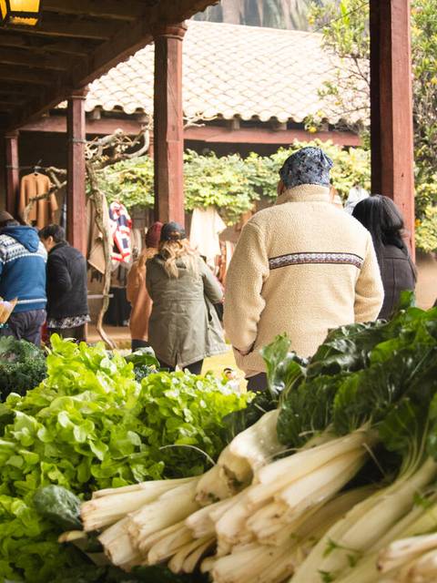 Una feria de agricultores con hortalizas frescas y personas comprando.