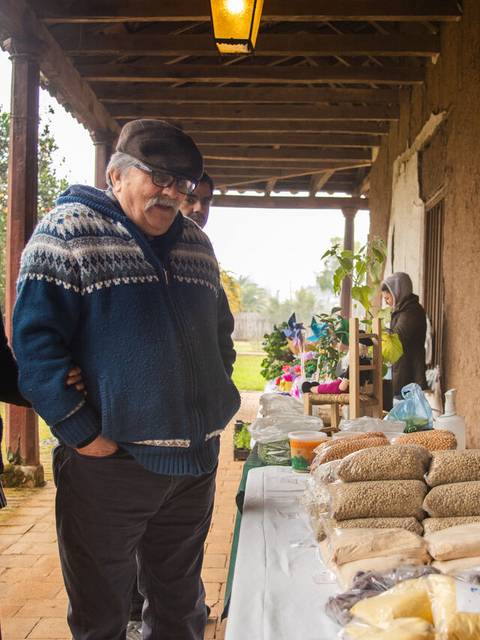 Un grupo de personas interactúa en un mercado al aire libre, observando productos locales en una mesa.