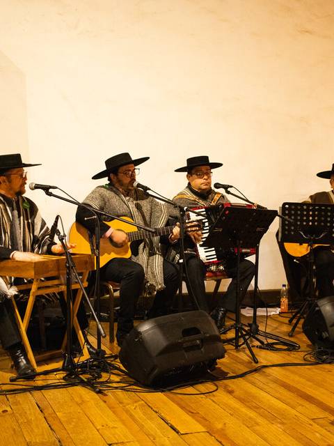 Cuatro músicos vestidos con ponchos y sombreros tocan instrumentos en un ambiente acogedor.