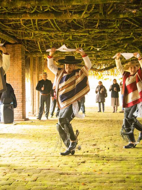 Tres bailarines en trajes tradicionales están realizando una danza folclórica en un espacio al aire libre.