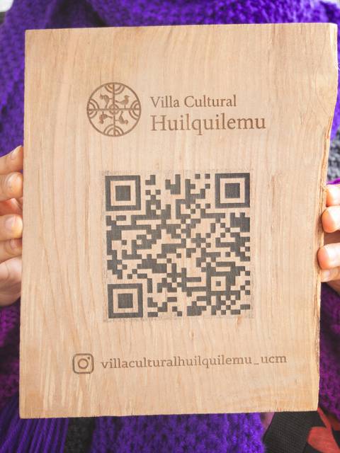 Una persona sostiene un cartel de madera con un código QR y el nombre de una villa cultural.