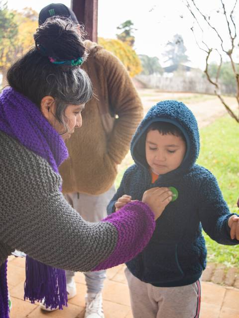 Un grupo de personas, incluida una mujer que viste un abrigo gris y un niño, están interactuando en un entorno al aire libre.