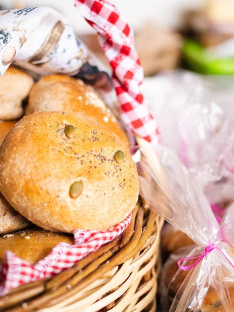 Una cesta de pan con bollos de masa integral, decorada con un paño a rayas rojas y blancas.