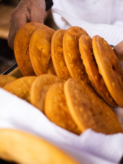 Un bandeja con varias tortillas doradas que están siendo sostenidas por manos.