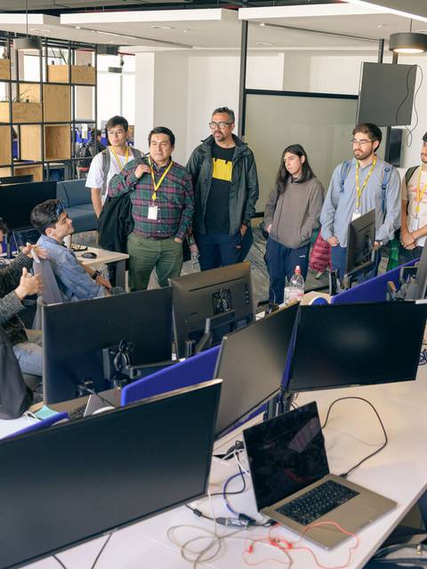 Un grupo de personas se reúne en un aula con computadoras para participar en una discusión o presentación.