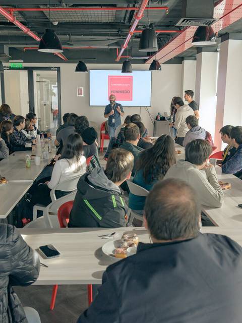 Una sala de conferencias con un grupo de personas sentadas y un presentador frente a una pantalla.
