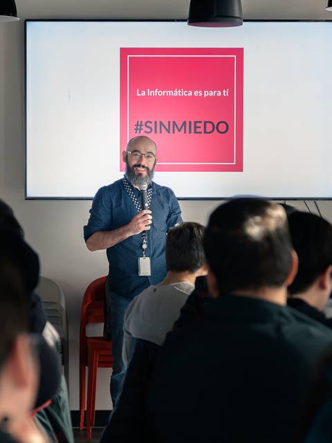 Un hablante presenta una charla sobre informática frente a una audiencia en un ambiente moderno.