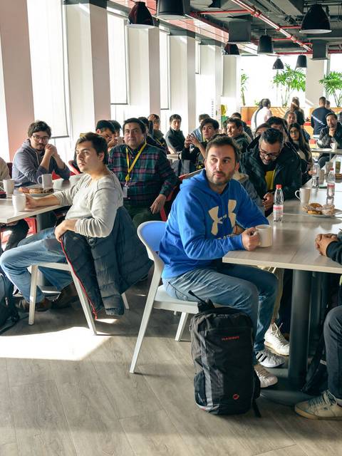Un grupo de personas sentadas en una cafetería conversando y disfrutando de sus bebidas.