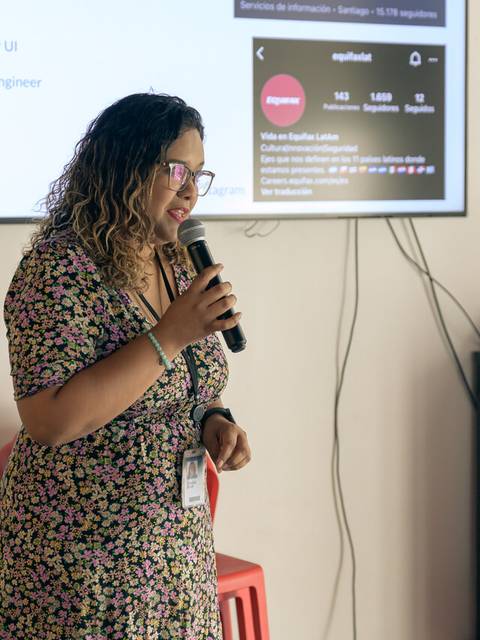Una mujer con cabello rizado habla en un evento mientras sostiene un micrófono.