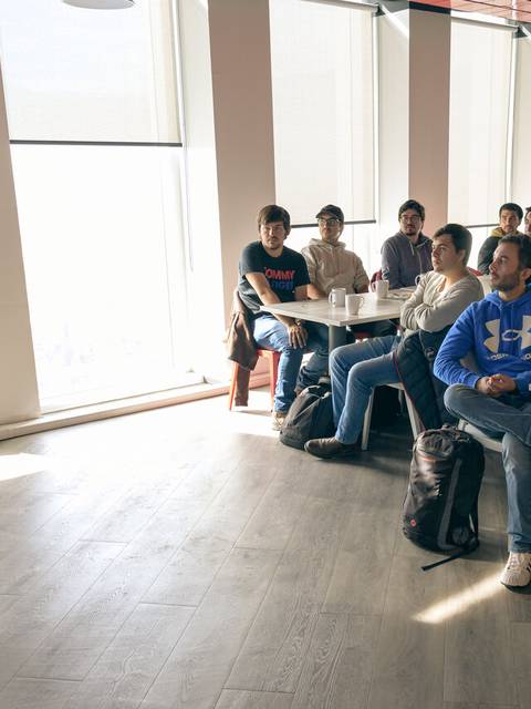 Una presentadora habla frente a un grupo de estudiantes en un salón luminoso.