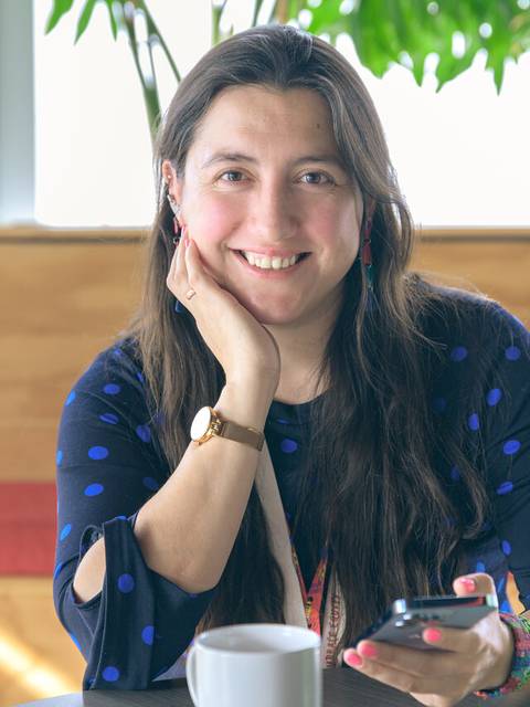Una mujer sonriente está sentada en una cafetería mirando su teléfono móvil.