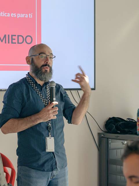 Un hombre con barba y gafas está dando una presentación sobre informática en un evento.