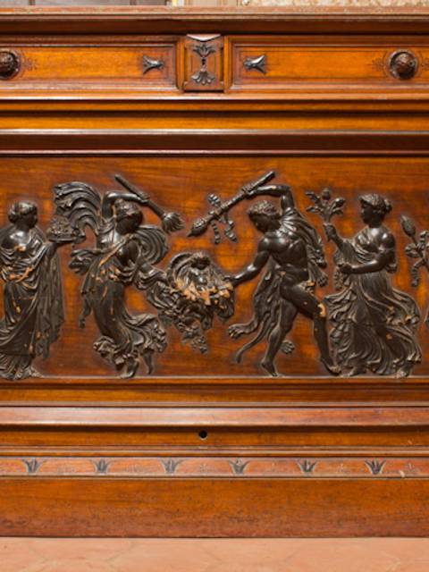 Una panel de madera con relieves metálicos que representan figuras humanas en una escena decorativa.