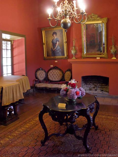 Sala decorada con muebles antiguos, cuadros en las paredes y un arreglo floral en la mesa.