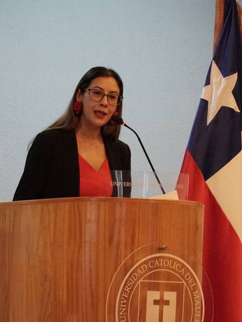 Una mujer habla en un podio frente a banderas chilena y de la universidad.