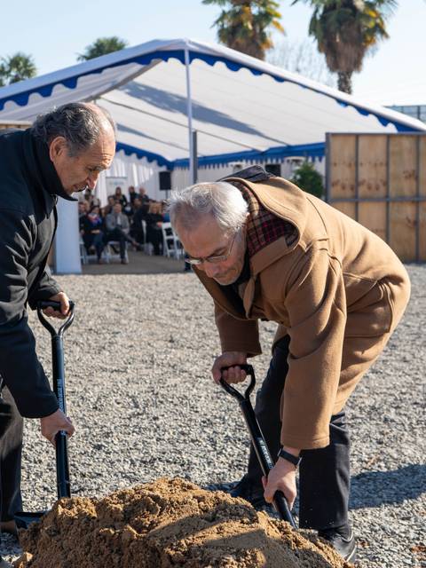 Dos hombres participan en una ceremonia de colocación de la primera piedra en un evento al aire libre.
