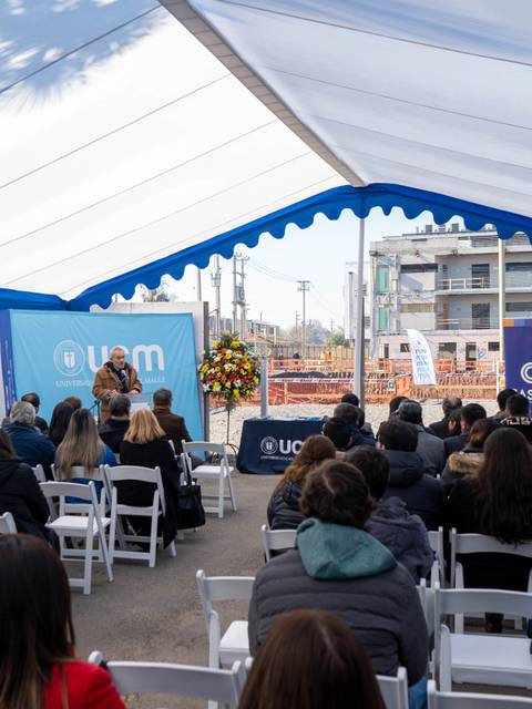 Un evento al aire libre bajo una carpa, con un público sentado y un escenario al fondo.
