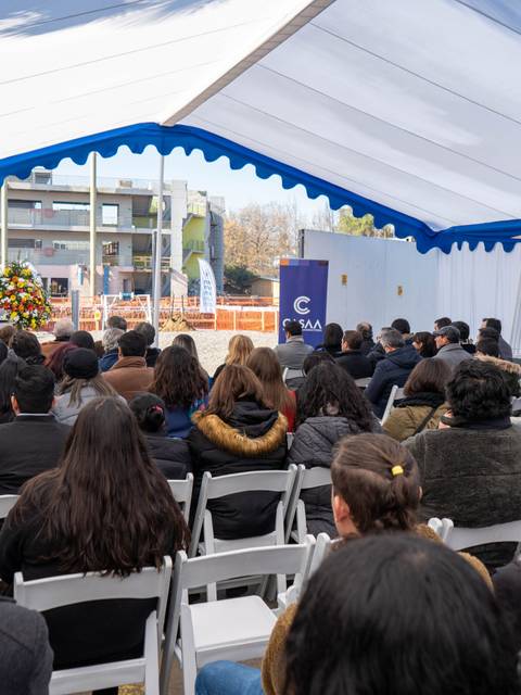 La imagen muestra a un grupo de personas asistiendo a un evento bajo una carpa, con un banner de UCM al fondo.
