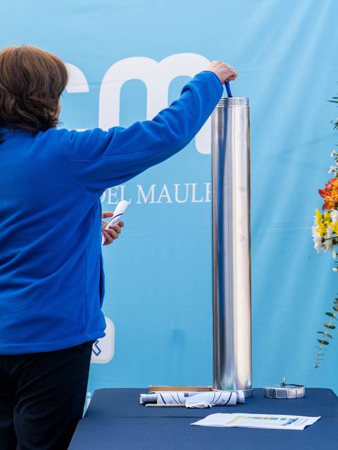 Una persona está realizando una actividad en una ceremonia junto a un cilindro metálico frente a un fondo decorado.