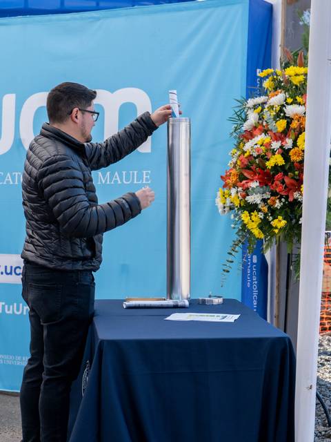 Un hombre está colocando un objeto en un soporte mientras se encuentra junto a un arreglo floral.