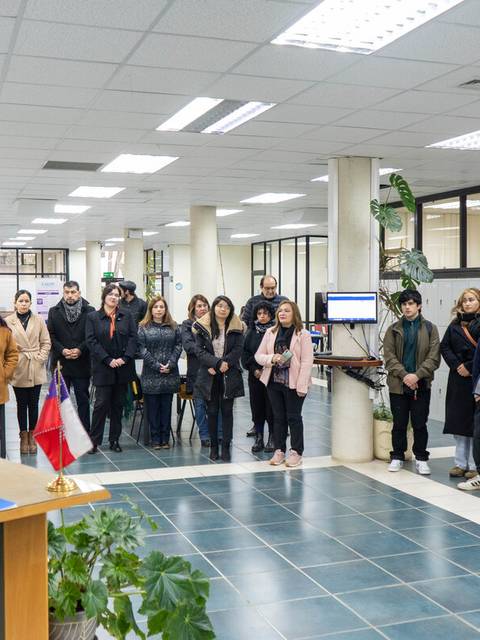 Una reunión con un grupo de personas en un espacio cerrado, donde una mujer habla desde un podio.