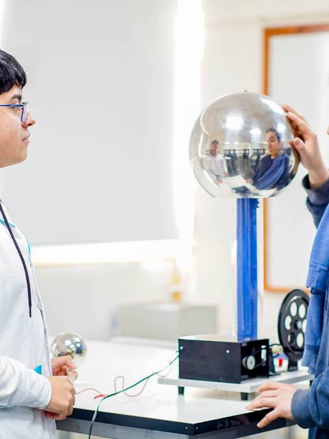 Dos estudiantes observan un experimento de electrostática con una esfera metálica.