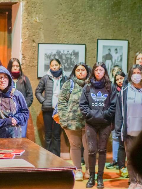 Un grupo de jóvenes escucha atentamente en un museo mientras observan fotografías en la pared.