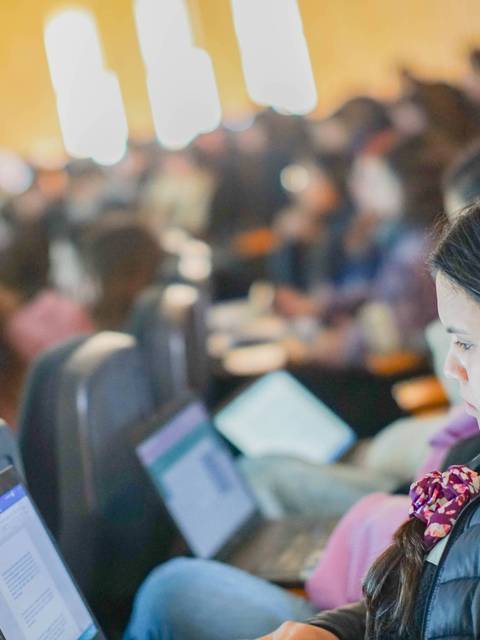 Un grupo de personas está en un aula utilizando computadoras portátiles.