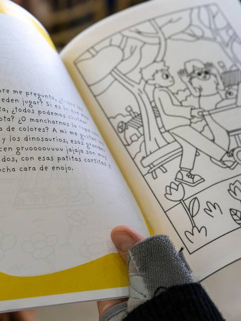 Una persona sostiene un libro abierto que contiene ilustraciones para colorear y texto en una de sus páginas.